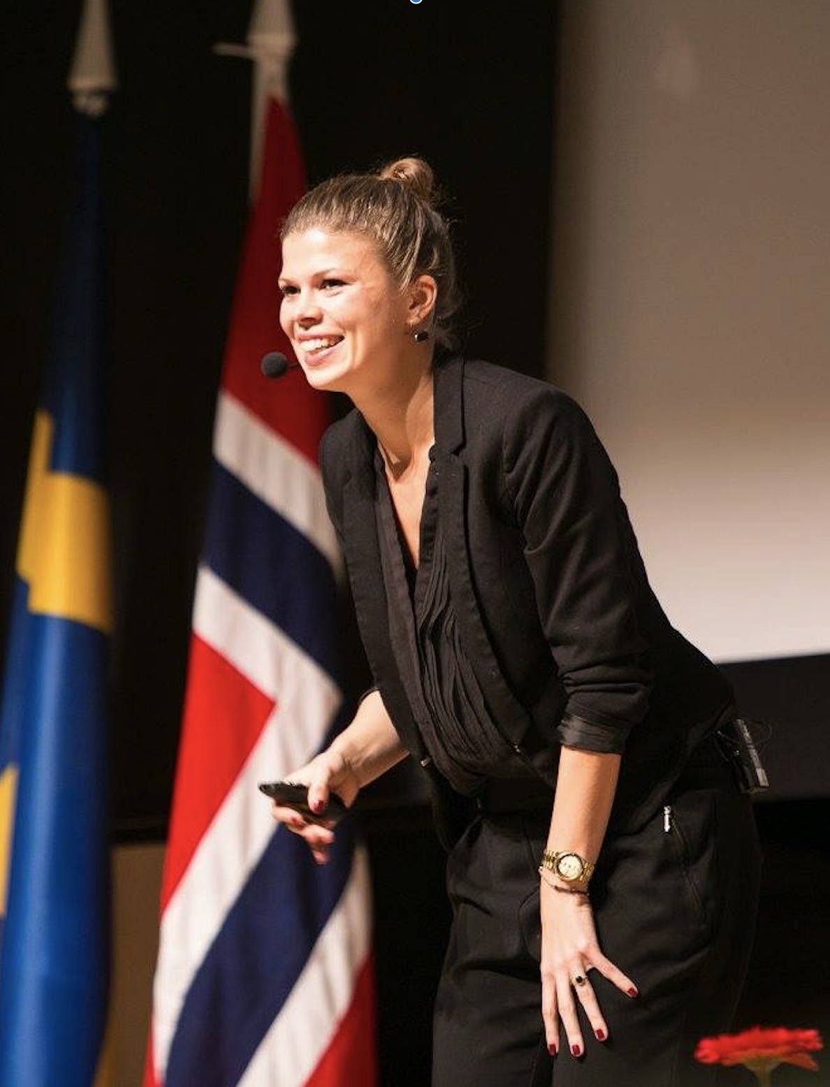Louise Fredbo-Nielsen holder foredrag om fremtidens trends og innovation på en international scene, iført sort outfit og med engageret kropssprog.